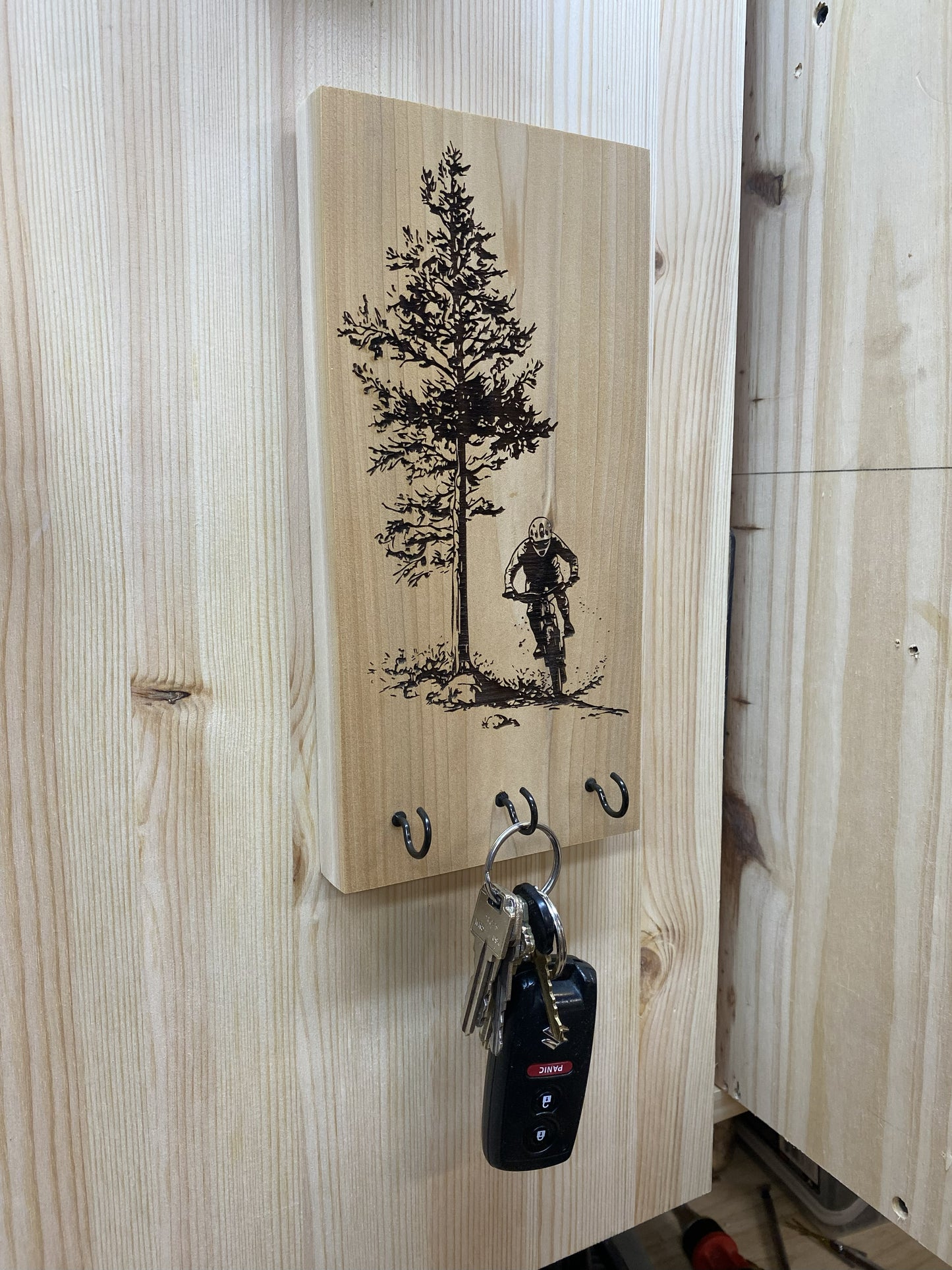Wooden wall hook with tree and mountain biker design, hanging on a wooden wall.