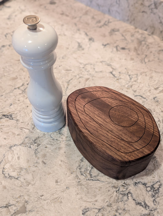 Wooden salt cellar with engraved topographic lines of Mt. Albert Edward with a pepper grinder on a marble surface