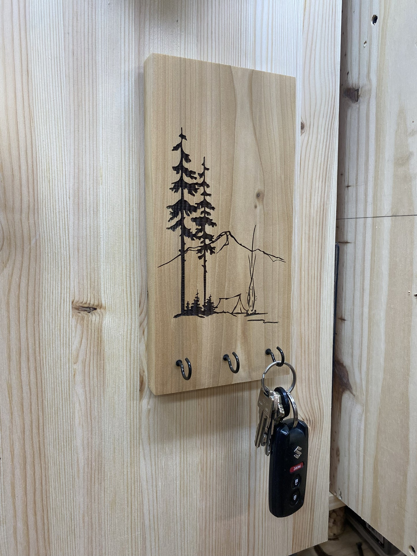 Wooden key holder with tree and mountain design on a wooden wall