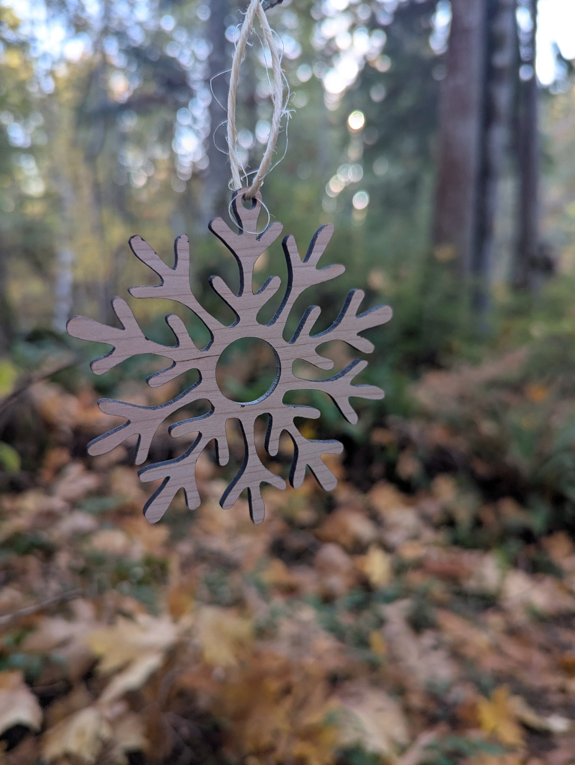 Handcrafted Wooden Snowflake Ornament hanging in a BC forest, ideal rustic Christmas decor.