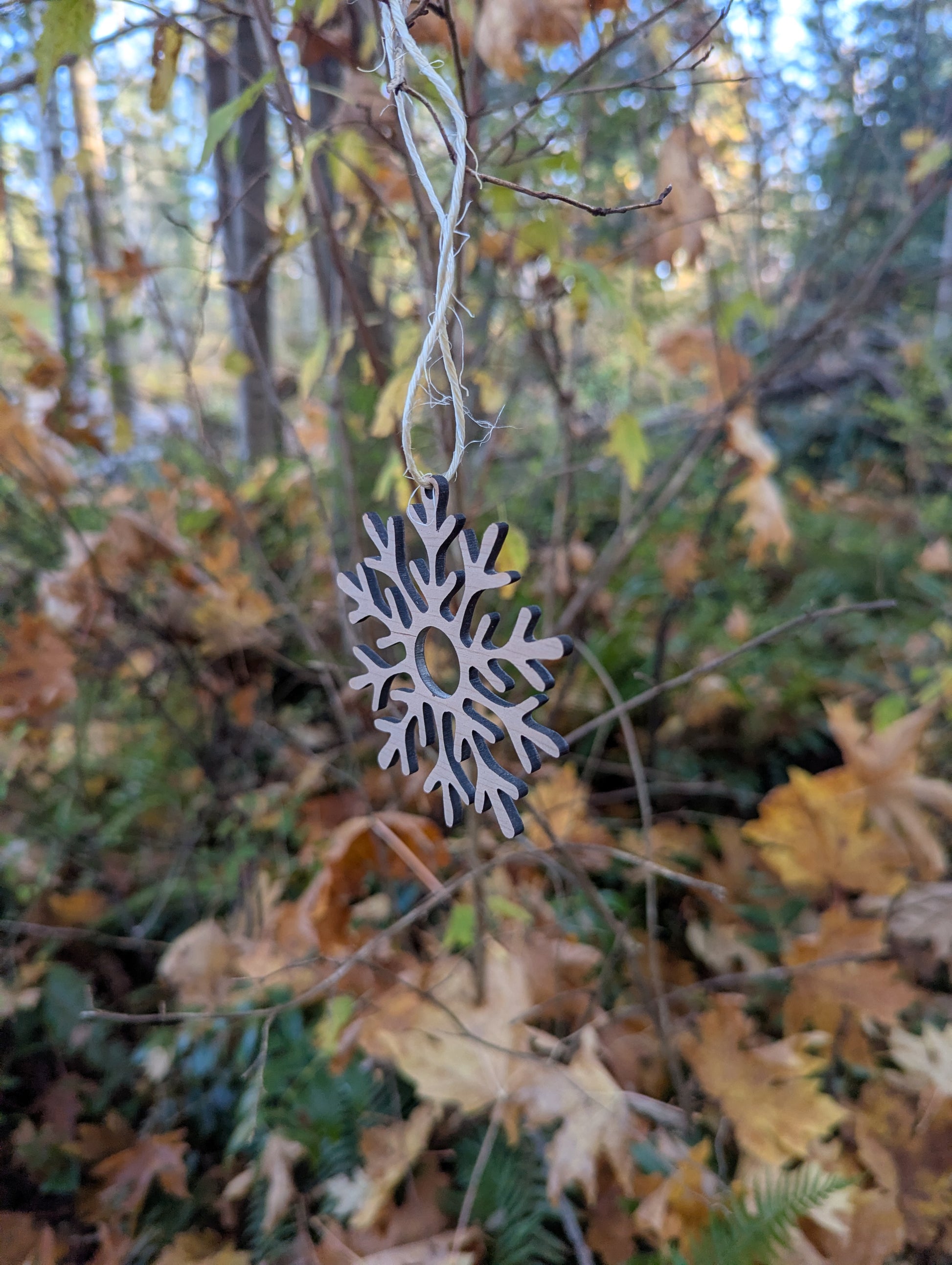 Handcrafted Wooden Snowflake Ornament hanging in a BC forest, ideal rustic Christmas decor.
