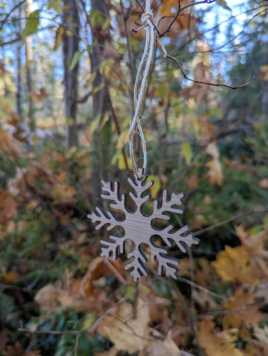 Handcrafted Wooden Snowflake Ornament hanging in a BC forest, ideal rustic Christmas decor.
